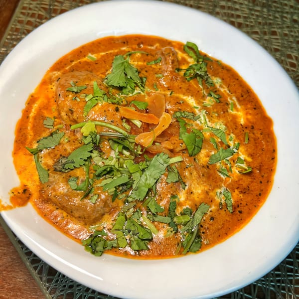 Indian butter chicken, garnished with fresh cilantro and cream, served in a white bowl.