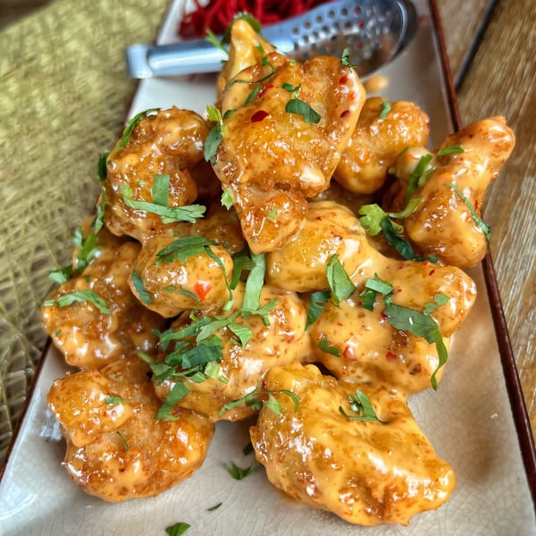 A plate of Mauka Indian Cuisine's crispy chicken pakora, coated in a creamy orange sauce and fresh herbs.