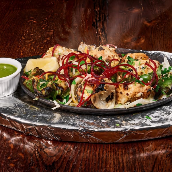 Sizzling Indian chicken tikka with onions, peppers, and red garnish, served with green chutney.