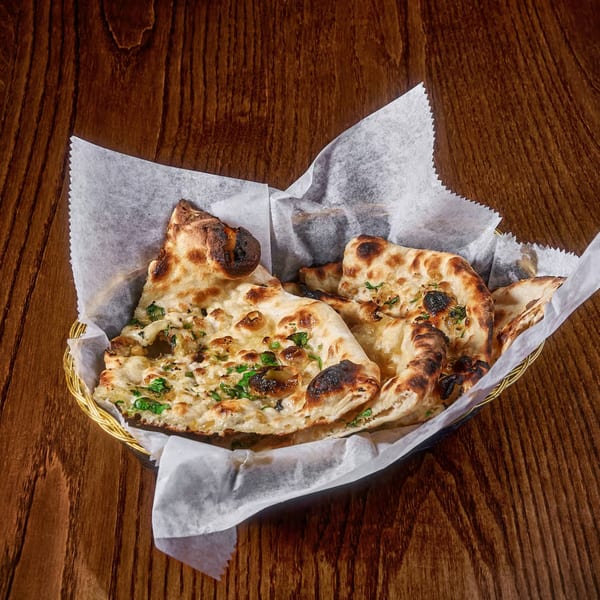 Golden brown garlic naan bread, garnished with cilantro, served in a basket on a wooden table.