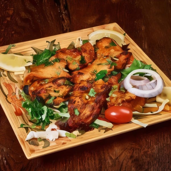 Indian chicken tikka with fresh greens, lemon, onion, and tomato on a wooden platter.