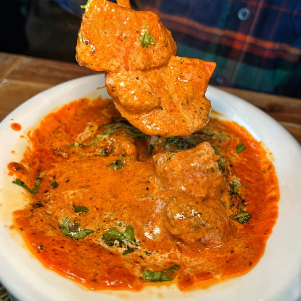 Chicken tikka masala, with a piece of chicken being lifted from a bowl of creamy orange sauce.